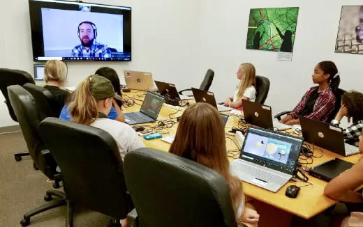 a group of people sitting around a table with laptops