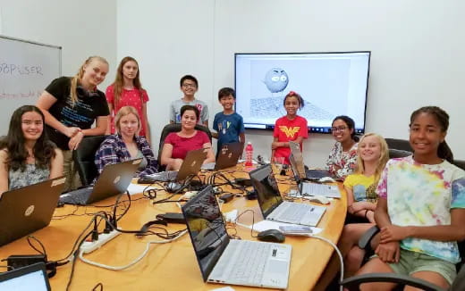 a group of people sitting around a table with laptops