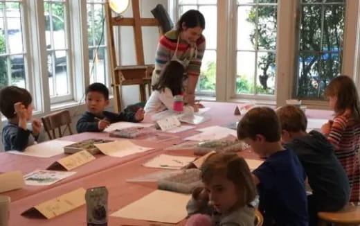 a person standing in front of a group of children sitting at a table