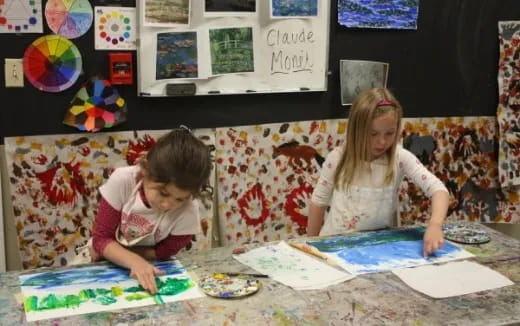 a couple of young girls sitting at a table with art on the wall