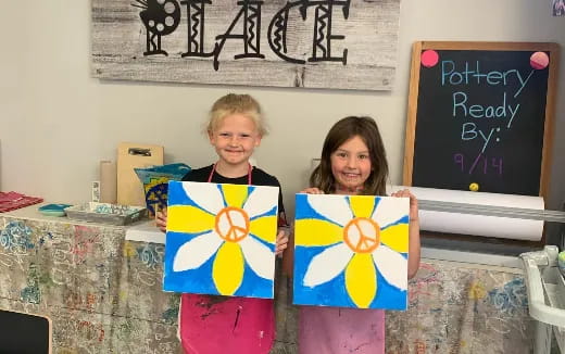 a couple of girls holding up paintings