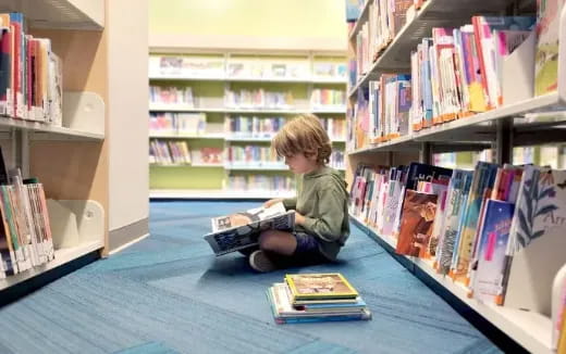 a child sitting on the floor reading a book in a library