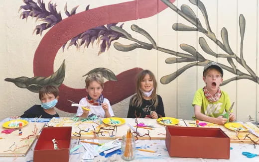 a group of children sitting at a table with a drawing on the wall