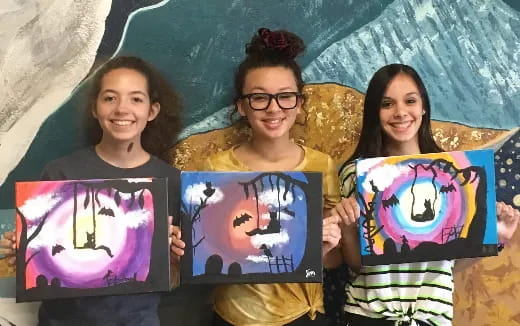 a group of girls holding up paintings