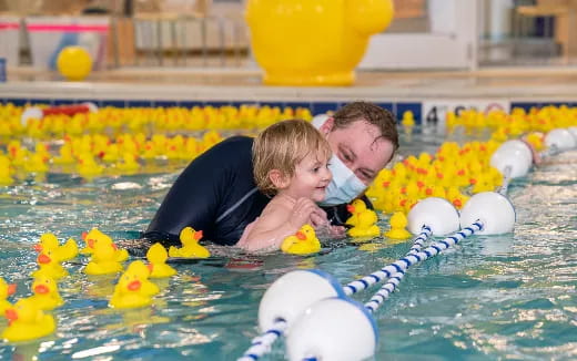 a person and a baby in a pool with rubber ducks