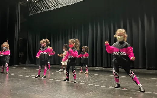 a group of girls in pink and black outfits dancing on a stage