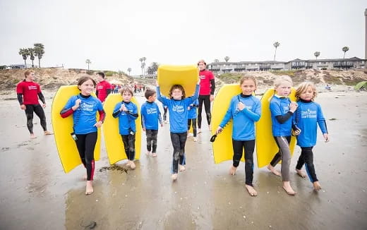 a group of kids carrying surfboards