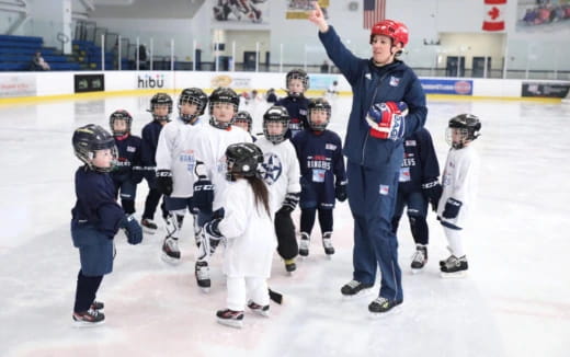 a man standing with a group of kids wearing helmets and holding up their hands