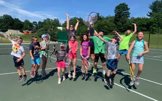 a group of kids holding tennis rackets on a court