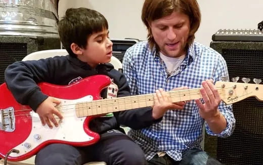 a person playing a guitar next to a boy