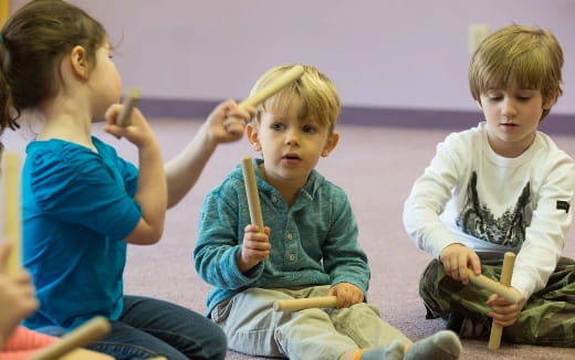 a group of children sitting on the floor holding sticks