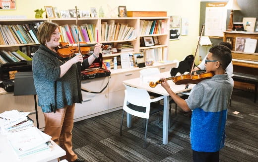 a woman playing a violin to a man sitting at a desk