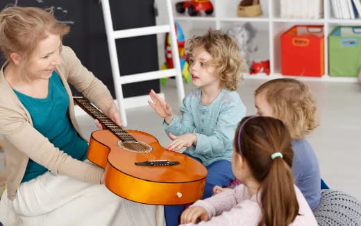 a woman playing a guitar to a group of children