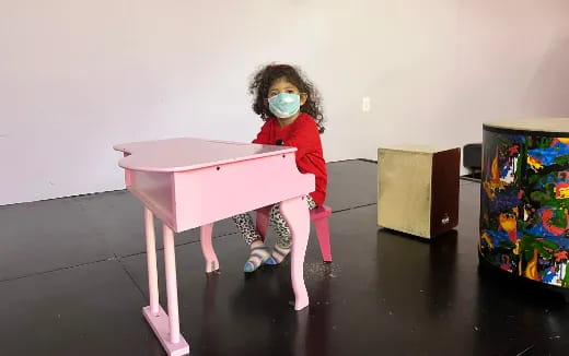 a girl wearing a mask and sitting on a pink table