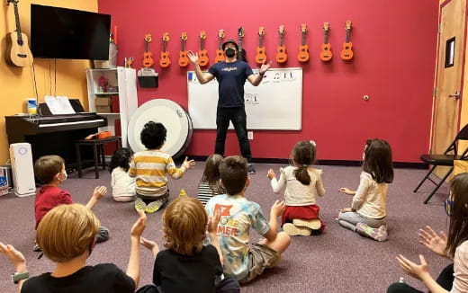 a group of children sitting in a circle in front of a person standing in front of a red