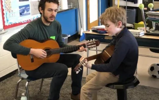 a person playing a guitar next to a boy sitting in a chair