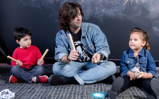 a person and two boys sitting on the floor holding sticks