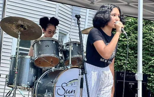 a woman singing into a microphone next to a man playing drums