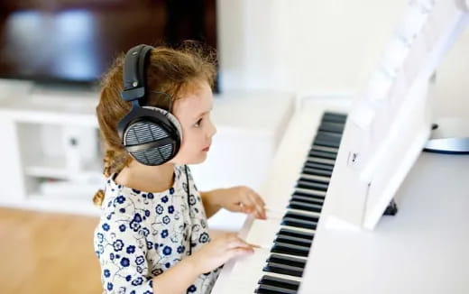 a young girl wearing headphones and playing a piano