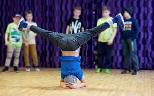 a person doing a handstand on a wood floor with other people in the background