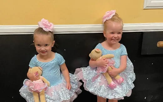 a couple of girls sitting on a bench with dolls