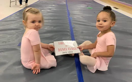 two young girls sitting on the floor holding a sign