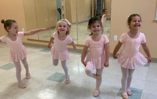 a group of girls wearing pink dresses and dancing in a room