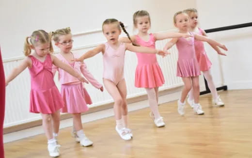 a group of girls in pink dresses dancing on a wood floor