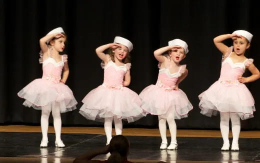 a group of girls wearing white dresses and hats on a stage