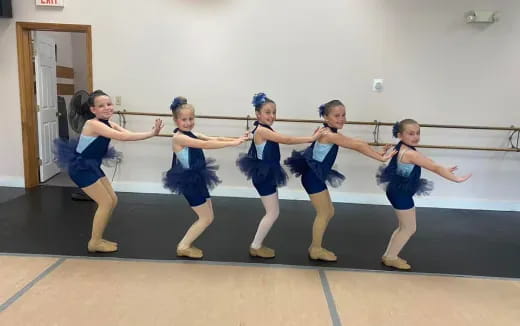 a group of girls in blue uniforms dancing on a wood floor