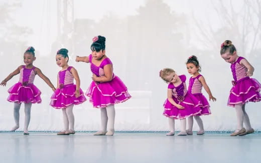 a group of girls wearing dresses and dancing on a stage