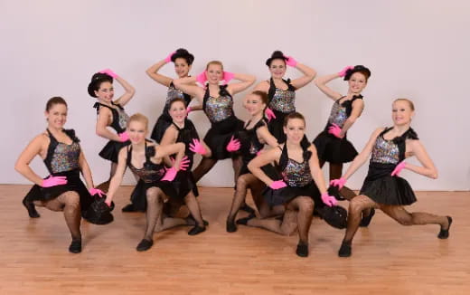 a group of women in black and pink dancing on a wood floor