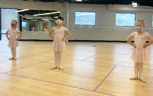 a group of girls wearing white dresses and masks on a wooden floor