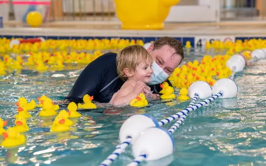 a person and a baby in a pool with rubber ducks