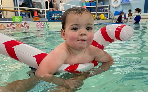 a boy in a pool with a toy in his mouth