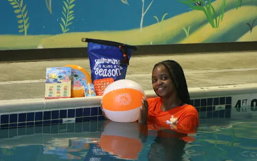 a person in a pool with a large orange ball and a bucket of water