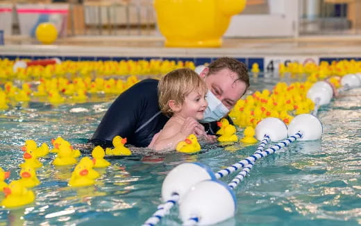 a person and a baby in a pool with rubber ducks