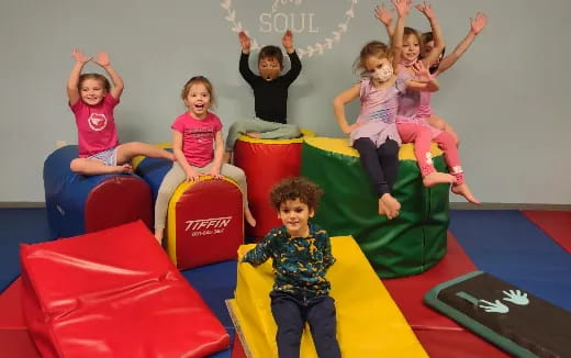 a group of children jumping on colorful chairs