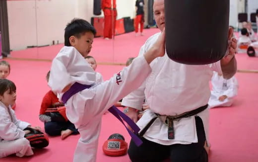 a person in a karate uniform holding a black ball in front of a boy in a white shirt