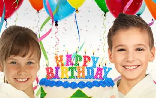a couple of kids smiling with a birthday cake in the background