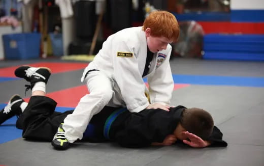 a person in a karate uniform kneeling down next to a person in a white uniform