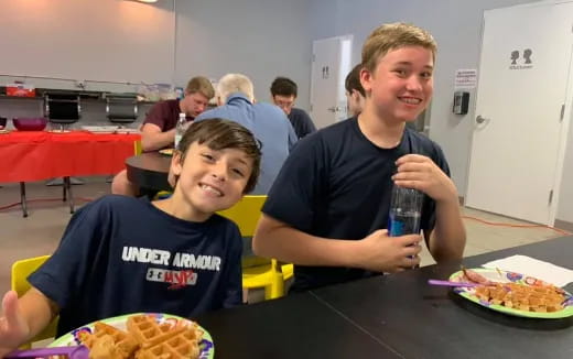 a couple of boys sitting at a table with food and drinks