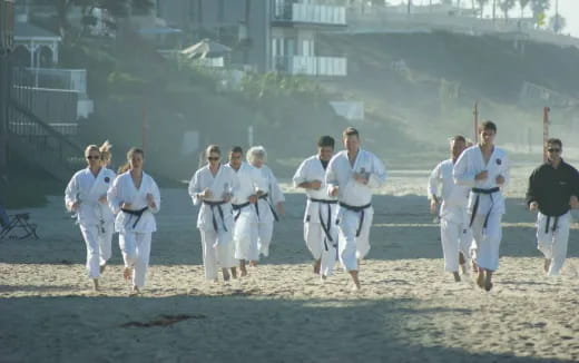 a group of people in white karate uniforms walking on a dirt field