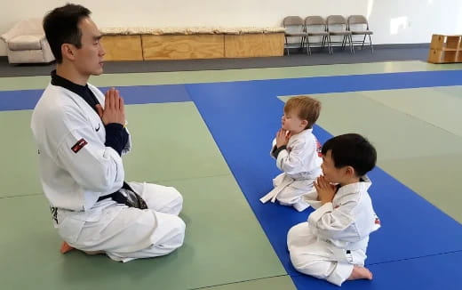a person and two boys in karate uniforms sitting on a blue mat