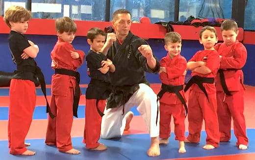 a person kneeling with a group of kids in red karate uniforms