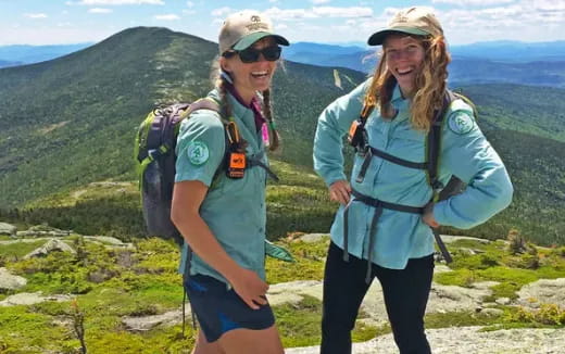 a couple of women with backpacks on a mountain