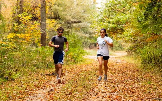 a man and woman running on a trail in the woods