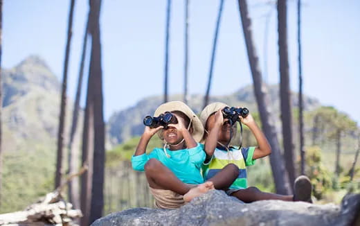 a person and a child sitting on a rock with binoculars