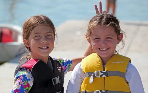 a couple of girls wearing life jackets and smiling at the camera