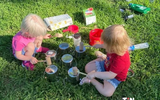 a couple of children sitting on the grass with a table and cups
